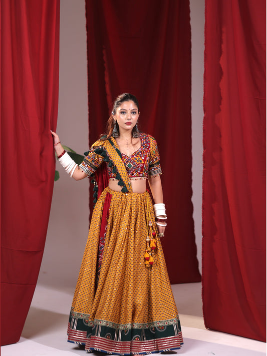 Front full-length view of a model wearing a mustard yellow cotton chaniya choli set featuring a geometric micro-print skirt with dark green arch borders and a multicolor embroidered blouse for Navratri garba.