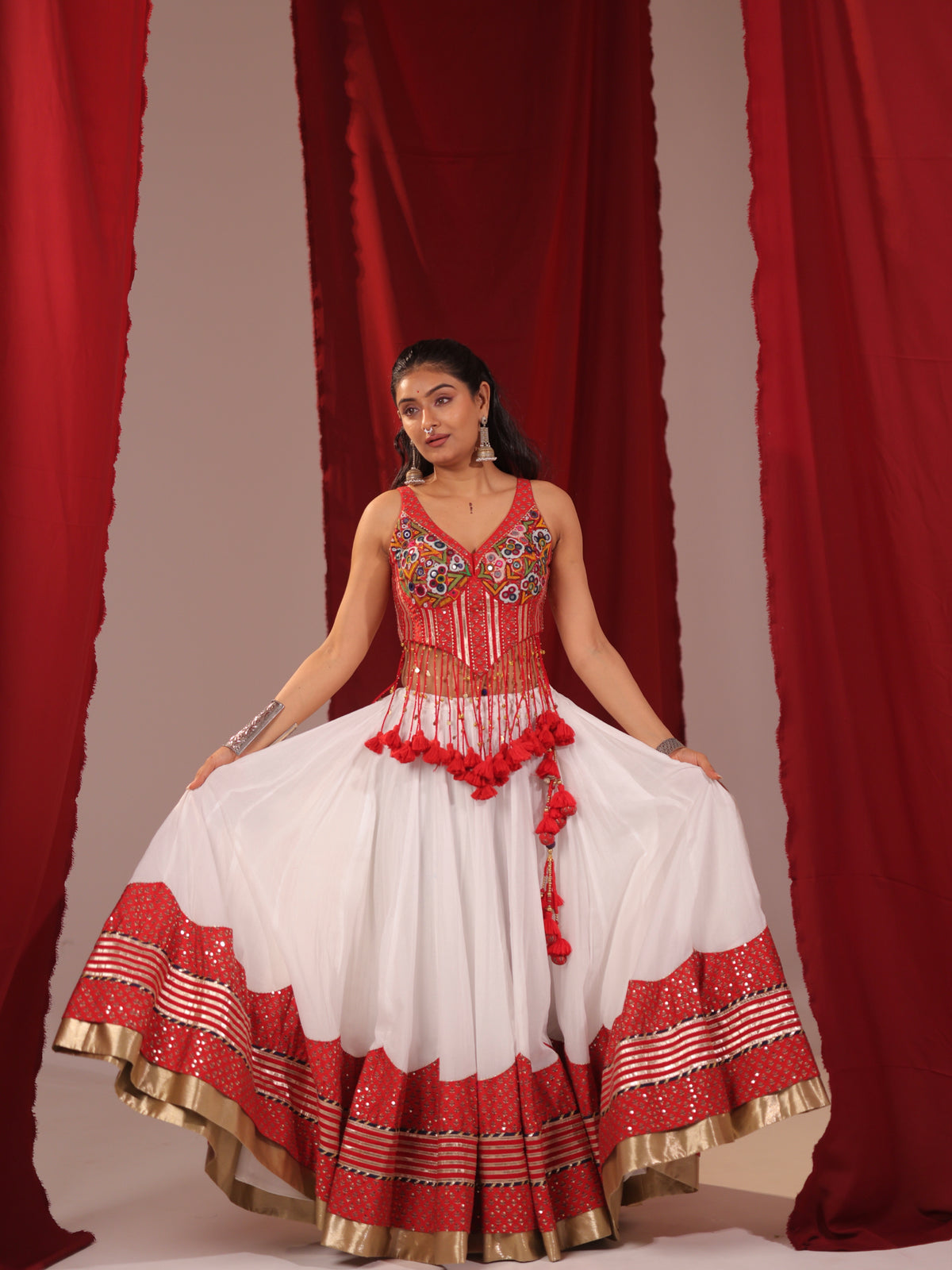 Front view of a model wearing a white and red cotton chaniya choli set with outstretched arms showcasing the voluminous flared skirt, red gota hemline, and embroidered corset choli for Navratri garba.